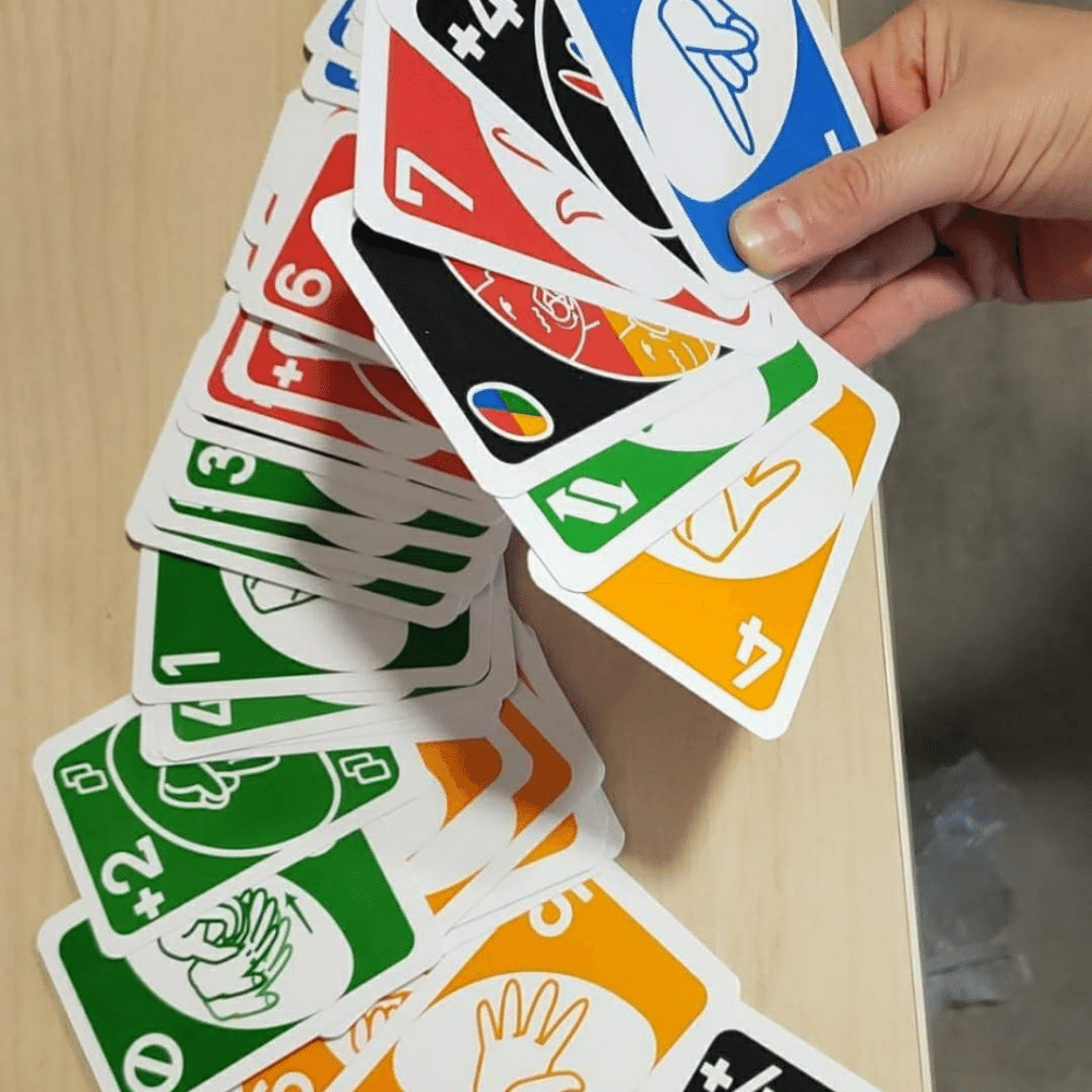 Foto de una persona sosteniendo varias carta del juego UNO en la mano y varias cartas más sobre la mesa