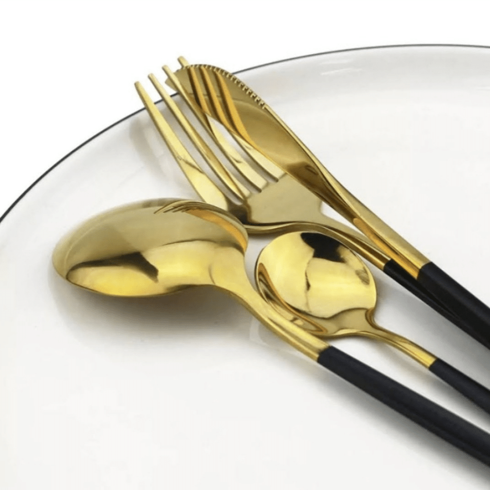 Sobre un plato blanco hay 4 cubiertos dorados con mando negro (cuchara grande, cuchara chica, tenedor, cuchillo)