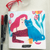 Foto, en el centro está la libreta con diseño de una mujer de pelo rosado con una gata azul sobre una mesa. Abajo dice Ilustrísima. Al lado de la libreta hay 2 lápices. Sobre la libreta un par de lentes.