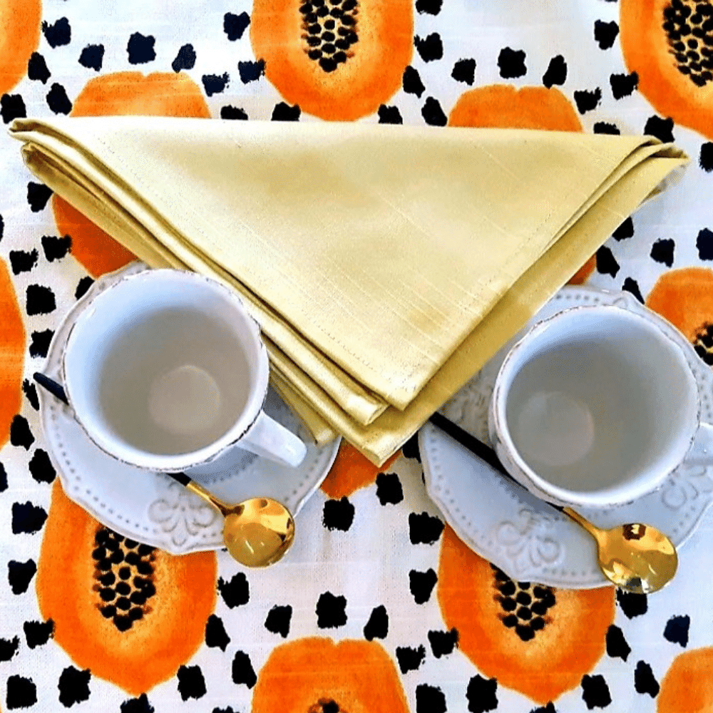 Imagen de un mantel con tazas y cubiertos, y arriba la servilleta dorada doblada