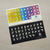 Foto de 2 adhesivos para teclado, uno de color negro con manos de una tonalidad amarilla, otro de varios color tonalidad arcoíris, con manos tonalidad amarilla
