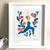 Fotografía de una cuadro con marco blanco con una ilustración de una mujer, con enterito ajustado azul, haciendo una posición de yoga con una pierna hacia adelante y otra hacia atrás, con brazos levantados y palmas juntas. De fondo varias flores. 